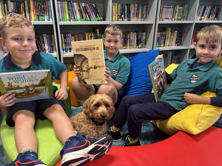 3 boy students reading books in the Library with the support dog Miss honey